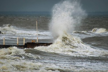 Fırtınalı havada dalgalı su ve liman. Büyük dalgalar rıhtıma çarpıyor. Küresel ısınmanın bir sonucu olarak orta enlemlerde anormal derecede güçlü fırtınalar meydana geliyor..