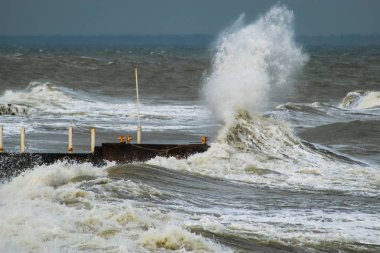 Fırtınalı havada dalgalı su ve liman. Büyük dalgalar rıhtıma çarpıyor. Küresel ısınmanın bir sonucu olarak orta enlemlerde anormal derecede güçlü fırtınalar meydana geliyor..