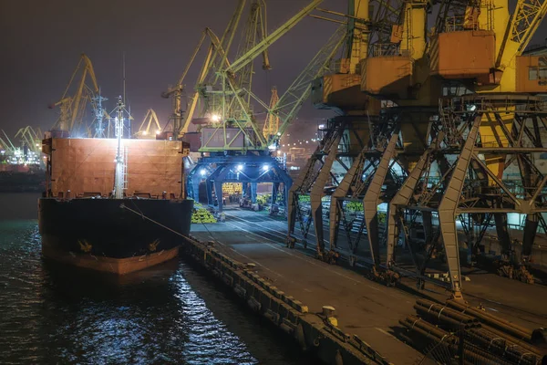 China. Cargo operation with bulk carrier vessel moored at pier. Big  cargo terminal at seaport. Cereals bulk transshipment from road transport to vessel at night.  Agricultural products transport.