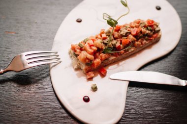 Somon balığı, taze sebzeler ve siyah arka planda çatal ve bıçaklı beyaz bir tabakta otlar. Restoran servisi.