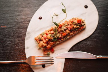 Somon balığı, taze sebzeler ve siyah arka planda çatal ve bıçaklı beyaz bir tabakta otlar. Restoran servisi.