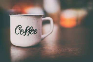 Enamel beyaz metal kupası. Üzerinde yazılı kahve yazılı. Arka planda bulanık tahta masa. Metin veya reklam için yer