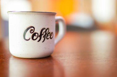 Enamel beyaz metal kupası. Üzerinde yazılı kahve yazılı. Arka planda bulanık tahta masa. Metin veya reklam için yer