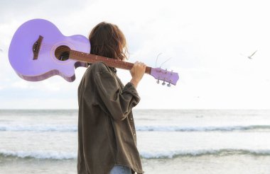 Sahilde akustik gitarlı çekici hippi kız denizin arka planında.