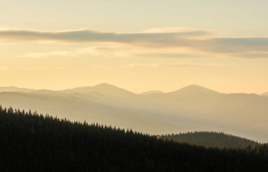 Dağların ve kaya siluetlerinin üstündeki şafak vakti sıcaklığı. Karanlık kayalıkları ve turuncu gündoğumu gökyüzü olan canlı bir dağ manzarası. Minimalist dağ manzarası ile kayalık dağların silueti