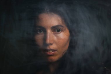 Siyah saçlı, esrarengiz bakışlı, siyah arka planda düşük ışıkta kameraya poz veren kadın portresi. Antika efekt ve eski tarz.