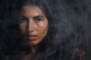 Siyah saçlı, esrarengiz bakışlı, siyah arka planda düşük ışıkta kameraya poz veren kadın portresi. Antika efekt ve eski tarz.