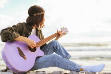 Sahilde arka planda akustik gitar çalan çekici hippi kız.
