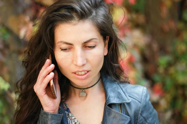 Sonbahar bahçesinde endişeli yüzlü şirin bir kız telefonda konuşuyor. Esmer kadın dışarıda cep telefonuyla konuşuyor..