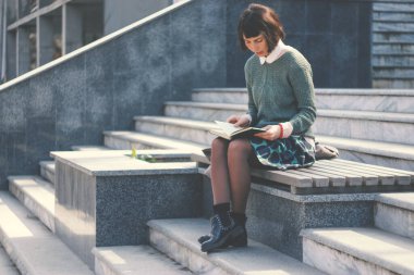 Genç kız öğrenci merdivenlerde kitap okur. Tam boy yaşam tarzı portresi. Genç Avrupalı bir kadın merdivenlerde oturuyor ve sınavlara hazırlanıyor..