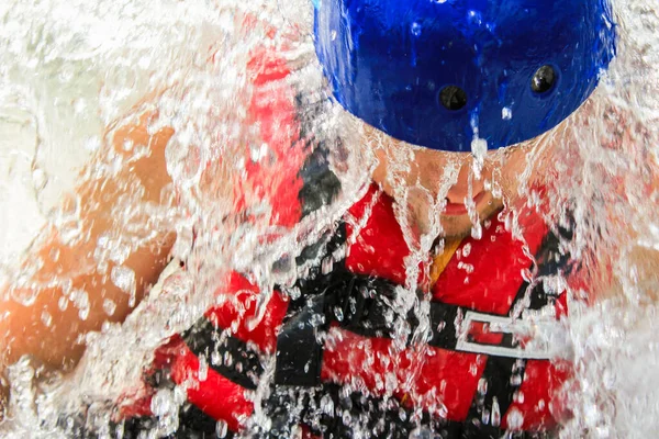 Close-up strong man in red life jacket and blue helmet in drops of water. Concept: extreme sports, rafting, outdoor activities, people in extreme situations.