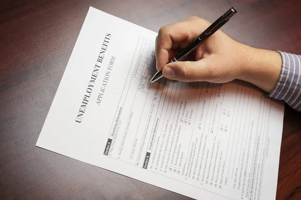 Close-up of a person's hand filing social security benefits application form.  Concept of Covid-19 coronavirus and stay at home order impact on economy, world economic crisis, unemployment.