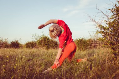 Kırmızı tayt giyen genç sarışın kadın yazın dışarıda akşam egzersizi yapıyor. Fitness yogası esneme antrenmanı dışarıda. Sağlıklı yaşam konsepti. Aktif yaşam biçimi