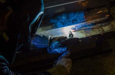 Metal ve kıvılcımlar üreten koruyucu maskeli kaynakçı.