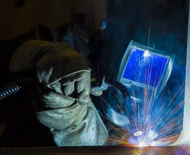 Metal ve kıvılcımlar üreten koruyucu maskeli kaynakçı.