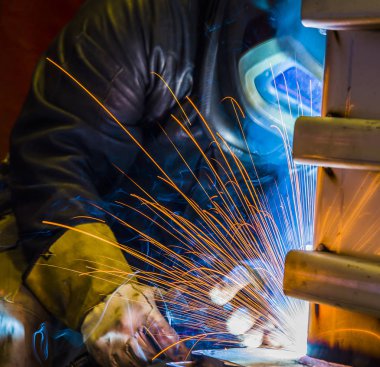 Metal ve kıvılcımlar üreten koruyucu maskeli kaynakçı.