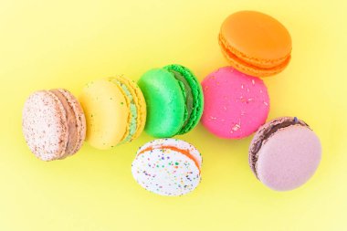 Pastel sarı arka planda tatlı renkli Fransız kurabiyeleri.