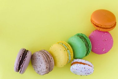 Pastel sarı arka planda tatlı renkli Fransız kurabiyeleri.