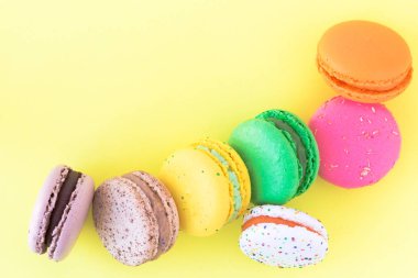 Pastel sarı arka planda tatlı renkli Fransız kurabiyeleri.