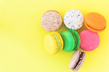 Pastel sarı arka planda tatlı renkli Fransız kurabiyeleri.