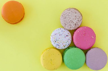 Pastel sarı arka planda tatlı renkli Fransız kurabiyeleri.