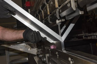 İşçi, atölyede metal baskı makinesi çalıştırıyor..