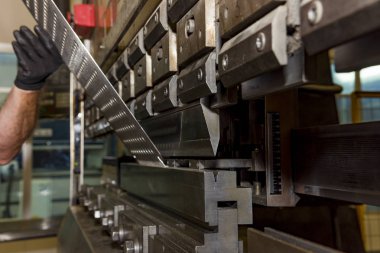 İşçi, atölyede metal baskı makinesi çalıştırıyor..