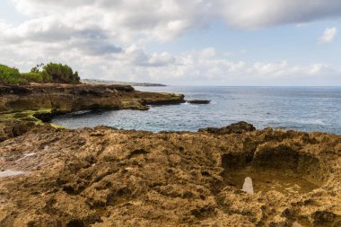 Nusa Lembongan, Bali, Endonezya 'daki Devil' s Tear 'da Rocky kıyı şeridi. Önünde gelgit havuzu olan kayalık bir sahil. Arkaplanda kıyı şeridi, okyanus, gökyüzü & bulutları. 