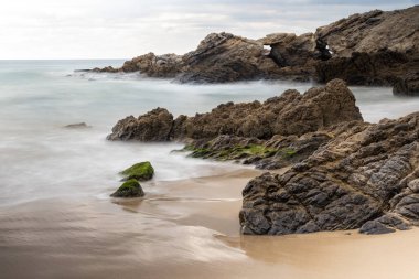 Leo Carrillo Sahili Malibu, California yakınlarında. Engebeli kıyı kayaları, pürüzsüz kumsal kumu, ötesinde ipeksi okyanus. Bulutlu gökyüzü. 