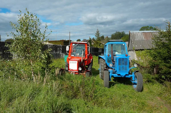 two tractors in a village near the wood house, red and blue trac
