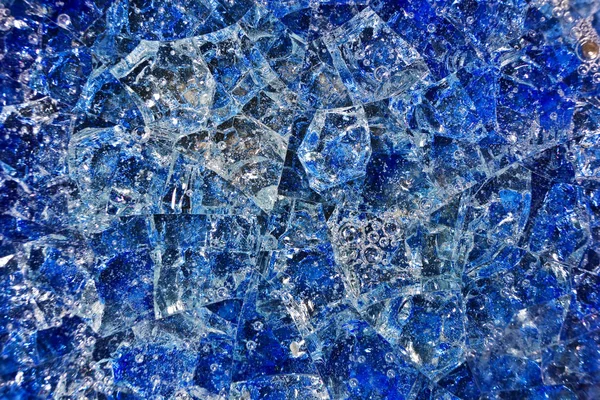 Blue broken glass with bubbles of air. Patterned background composed of yellow crystals and ceramics.