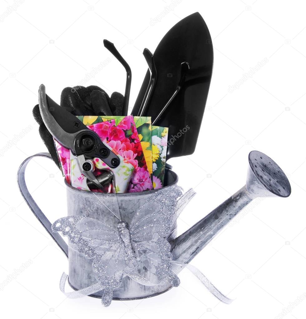 Composition of garden tools: silver watering can, colored shears in flowers, small black shoulder to the garden, small rake, gardening gloves, seed capsules of flowers.