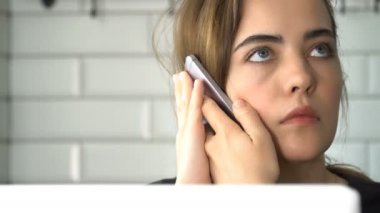 Kız Smartphone'da konuşuyor ve bir dizüstü bilgisayarda çalışıyor. Bir kadın evde, freelancing çalışıyor