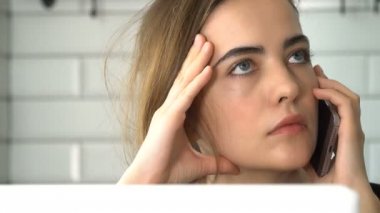 Kız Smartphone'da konuşuyor ve bir dizüstü bilgisayarda çalışıyor. Bir kadın evde, freelancing çalışıyor