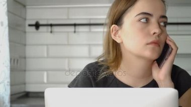 Kız Smartphone'da konuşuyor ve bir dizüstü bilgisayarda çalışıyor. Bir kadın evde, freelancing çalışıyor