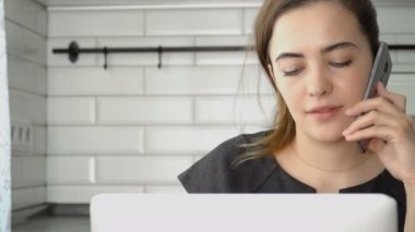 Kız kameraya bakıyor ve gülümsüyor. Kız bir smartphone üzerinde konuşmak ve bir dizüstü bilgisayar üzerinde çalışan