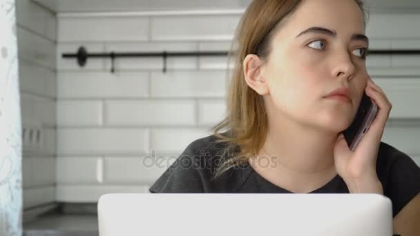 Kız Smartphone'da konuşuyor ve bir dizüstü bilgisayarda çalışıyor. Bir kadın evde, freelancing çalışıyor — Stok video