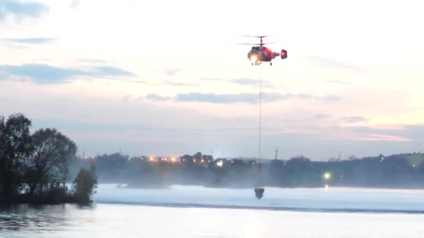 El helicóptero recoge agua en el río para extinguir un incendio. El servicio de rescate y los bomberos apagan el fuego. El helicóptero flotaba en el aire. Fuego en Moscú, Rusia. Helicóptero militar — Vídeo de stock