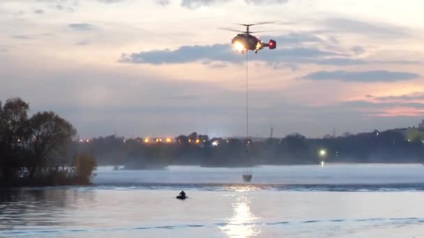 Hélicoptère du ministère des Situations d'urgence. L'hélicoptère recueille de l'eau dans la rivière pour éteindre un incendie. Le sauvetage — Video