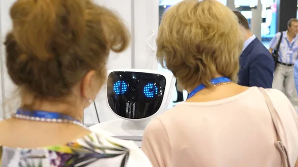 Робот общается с людьми. Взаимодействие робота и человека. Современные роботизированные технологии. Робот смотрит в камеру на человека. Робот показывает эмоции. Поднимает руки вверх. Стоковое Фото