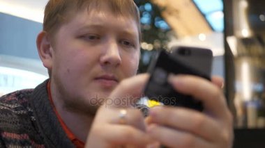 Alışveriş merkezi food court, sahil yolu şifre koyarak smartphone kullanarak delikanlı. Ücretli bir banka kartı ile online alışveriş için bir genç adam ve o mutlu ve gülümsüyor