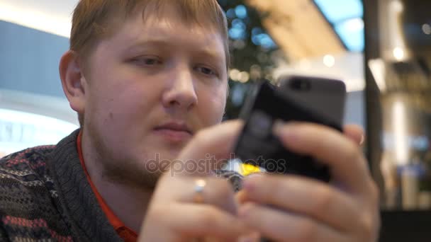 Los hombres jóvenes que utilizan el teléfono inteligente poner código promocional en el patio de comidas en el centro comercial. Un joven un pagado por compras en línea con una tarjeta bancaria y él es feliz y sonríe — Vídeos de Stock