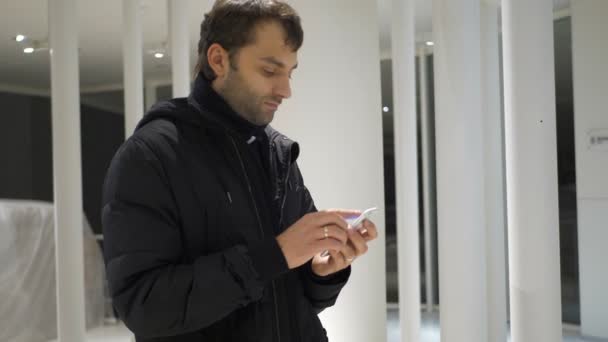 Смс-повідомлення людини, використовуючи додаток на смартфоні вночі в місті. Красивий молодий бізнесмен використовує смартфон, посміхаючись, щасливий одягнений піджак на відкритому повітрі. Міський чоловічий професіонал. руки, що друкують смс прокрутка — стокове відео