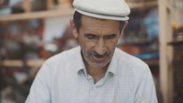 Yetişkin bir Müslüman adam portresi. Eski Müslüman kendi elleri ile ulusal geleneksel yemekleri yapar. Woodcarver atölyesinde çalışmak. Tahta kaşık bıçak ile yapım. Eski usta elleri. Kafkasya — Stok video