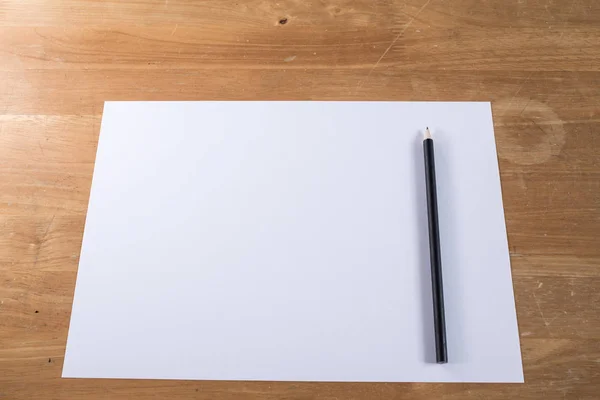 Dokument white paper s černou tužkou na dřevo stůl — Stock fotografie