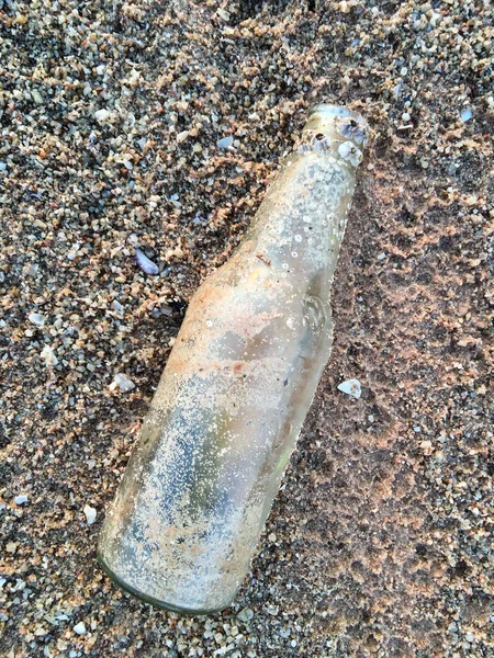 Стеклянная бутылка с раковиной на пляже, загрязнение пляжа — стоковое фото