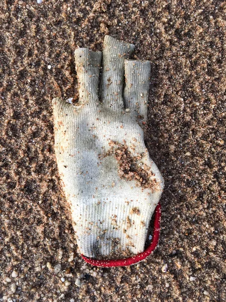 Грязная вязаная зимняя перчатка на пляже — стоковое фото