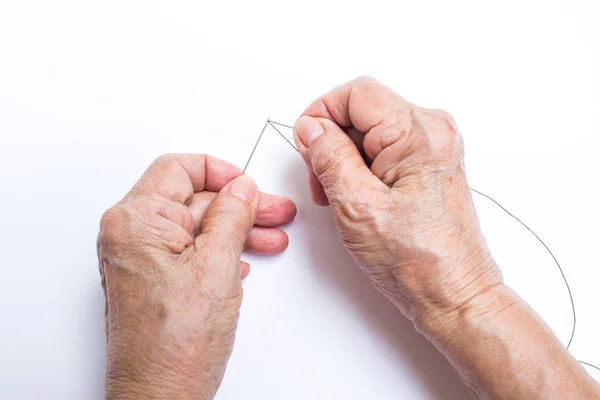 Руки пожилой женщины заканчивают нитку иглы, изолированной на белом фоне, О портном — стоковое фото