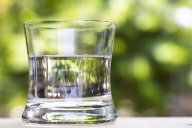 Transparent glass of clean water on wood table in bokeh green garden background, Close up & Macro shot, Selective focus, Healthy Drink concept