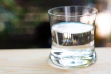 Bokeh bahçesinin arka planında, ahşap masanın üzerindeki temiz suyun bulanık bardağı, Makro şat ve Sağlıklı İçecek kavramını kapat